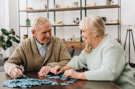 Two seniors sit at a table and work together to put a puzzle together.