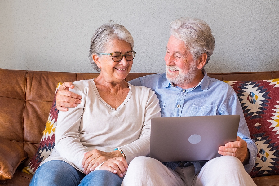 A senior couple sits on a couch together with a laptop