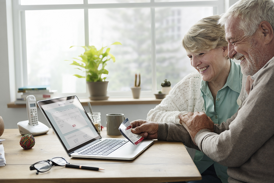 An older adult couple sits at a table looking at a laptop