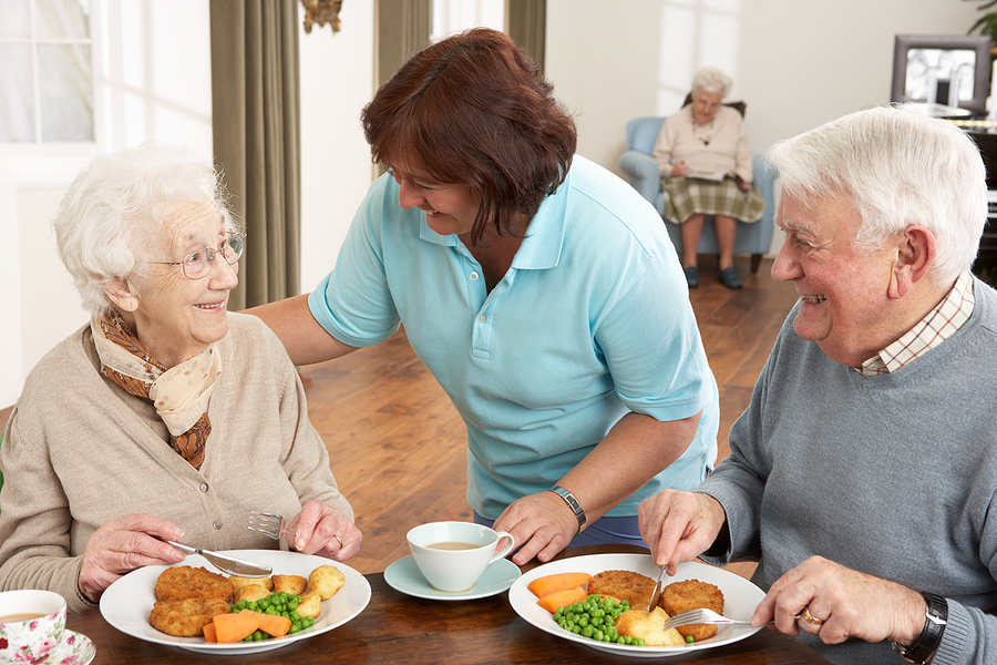 Two older seniors being served a meal in a dining room at a senior living community.