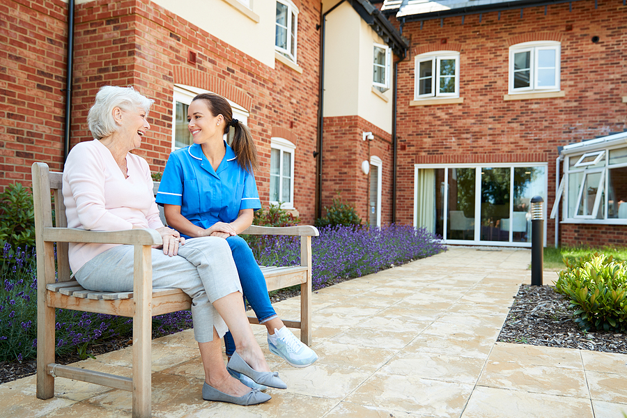 An older woman and a younger woman, sitting outside talking on a bench.