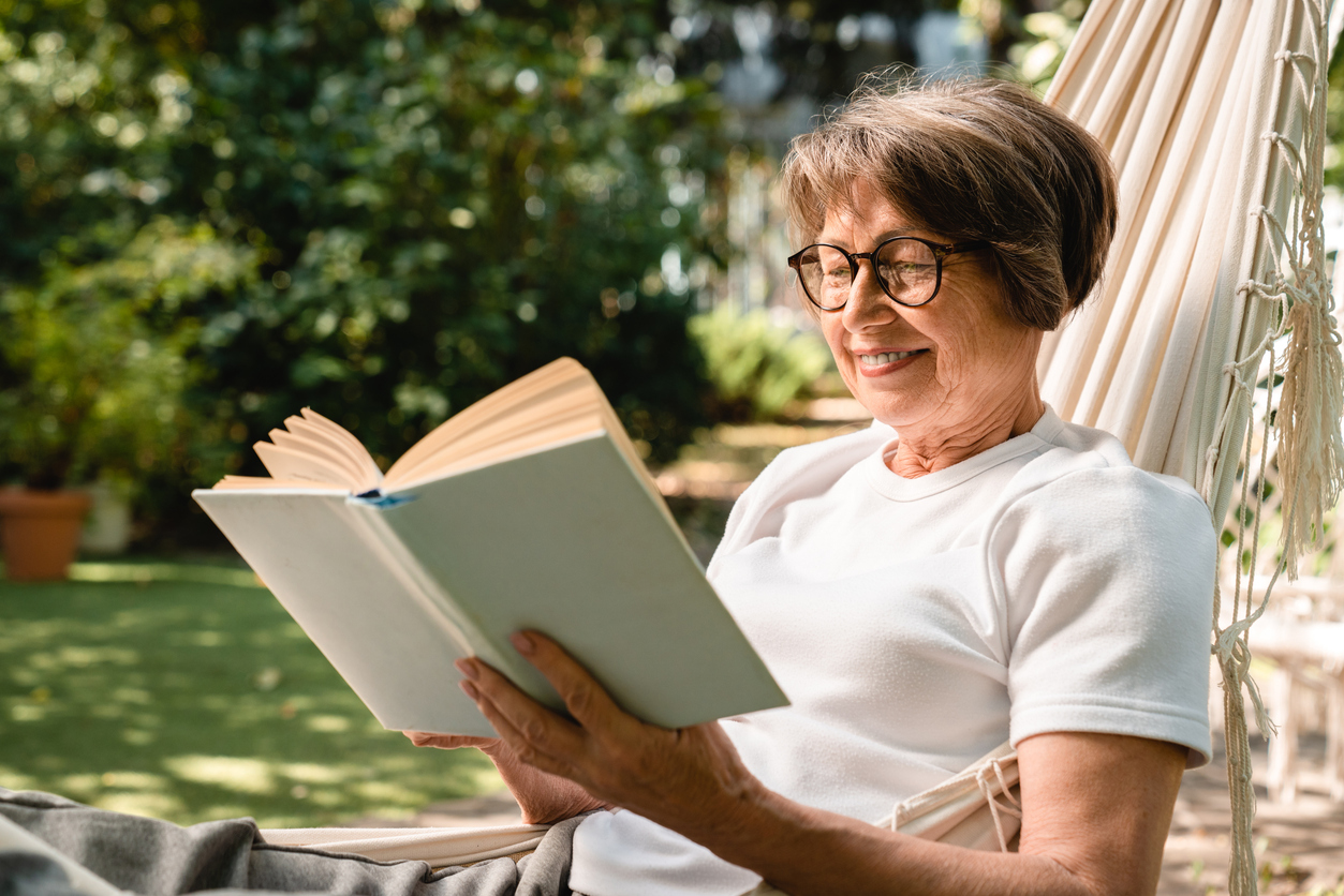 A senior woman reads a summer book in a hammock